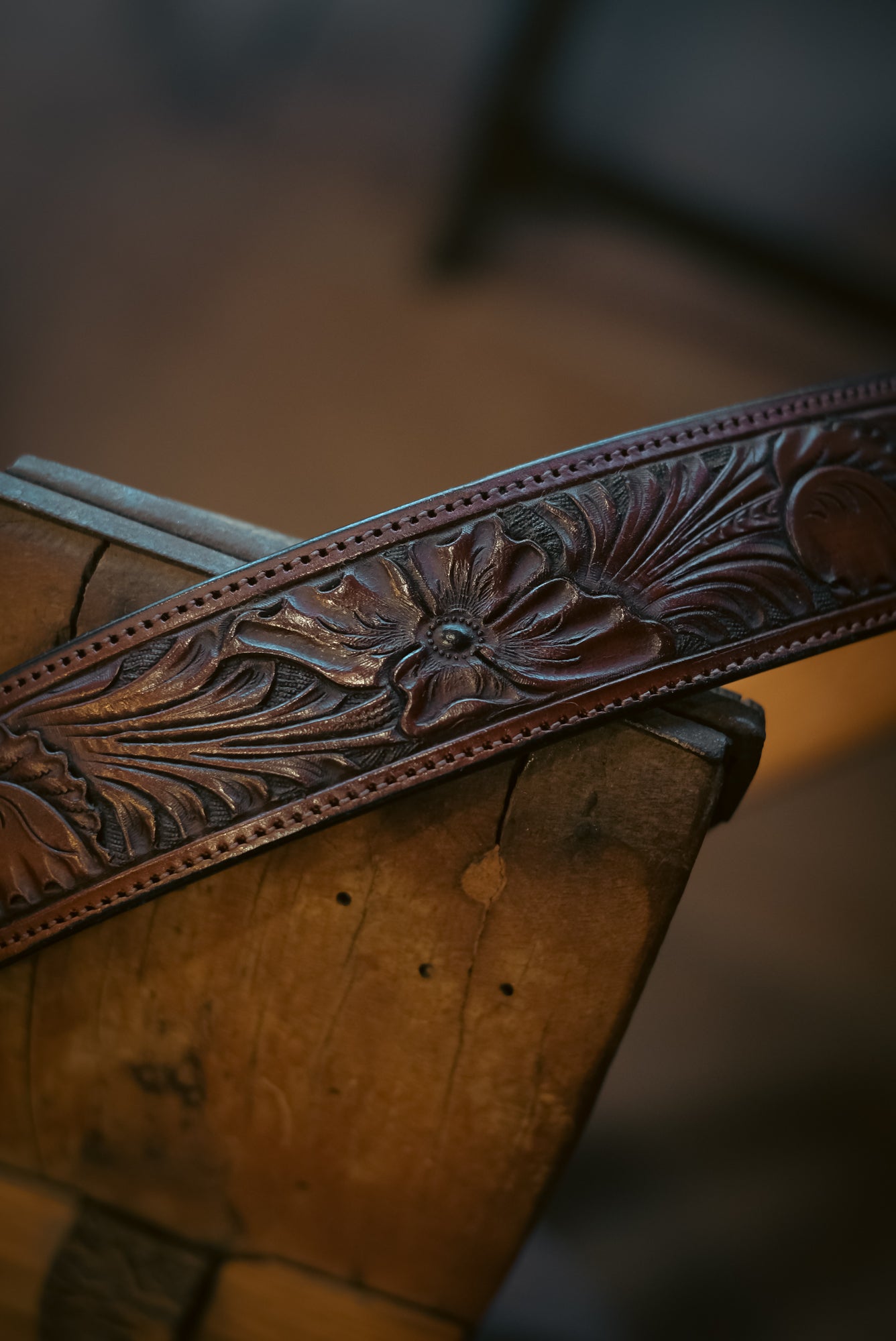 Close-up of a leather guitar strap with intricate floral patterns on a wooden surface.
