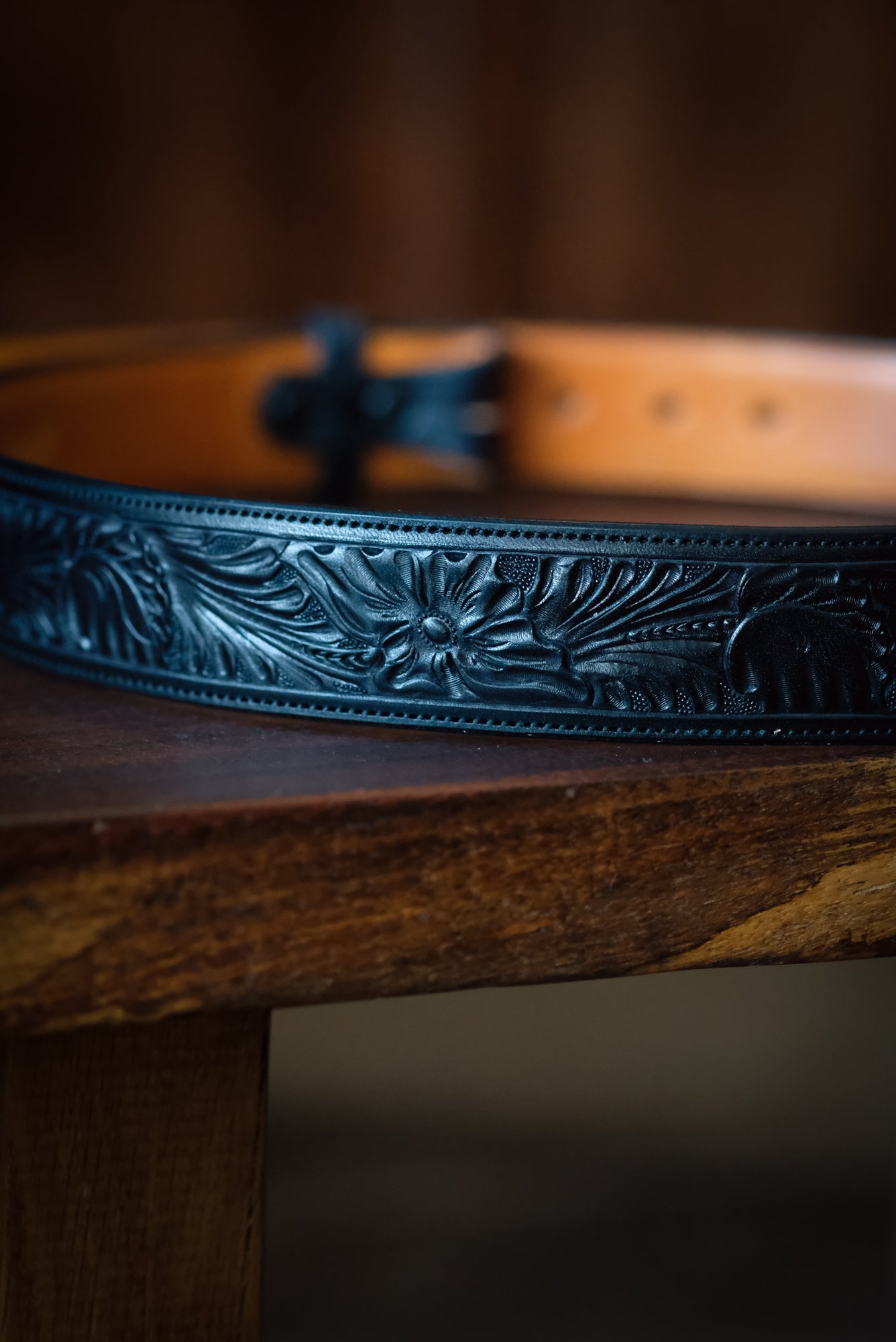 Black leather belt with floral embossing on a wooden surface
