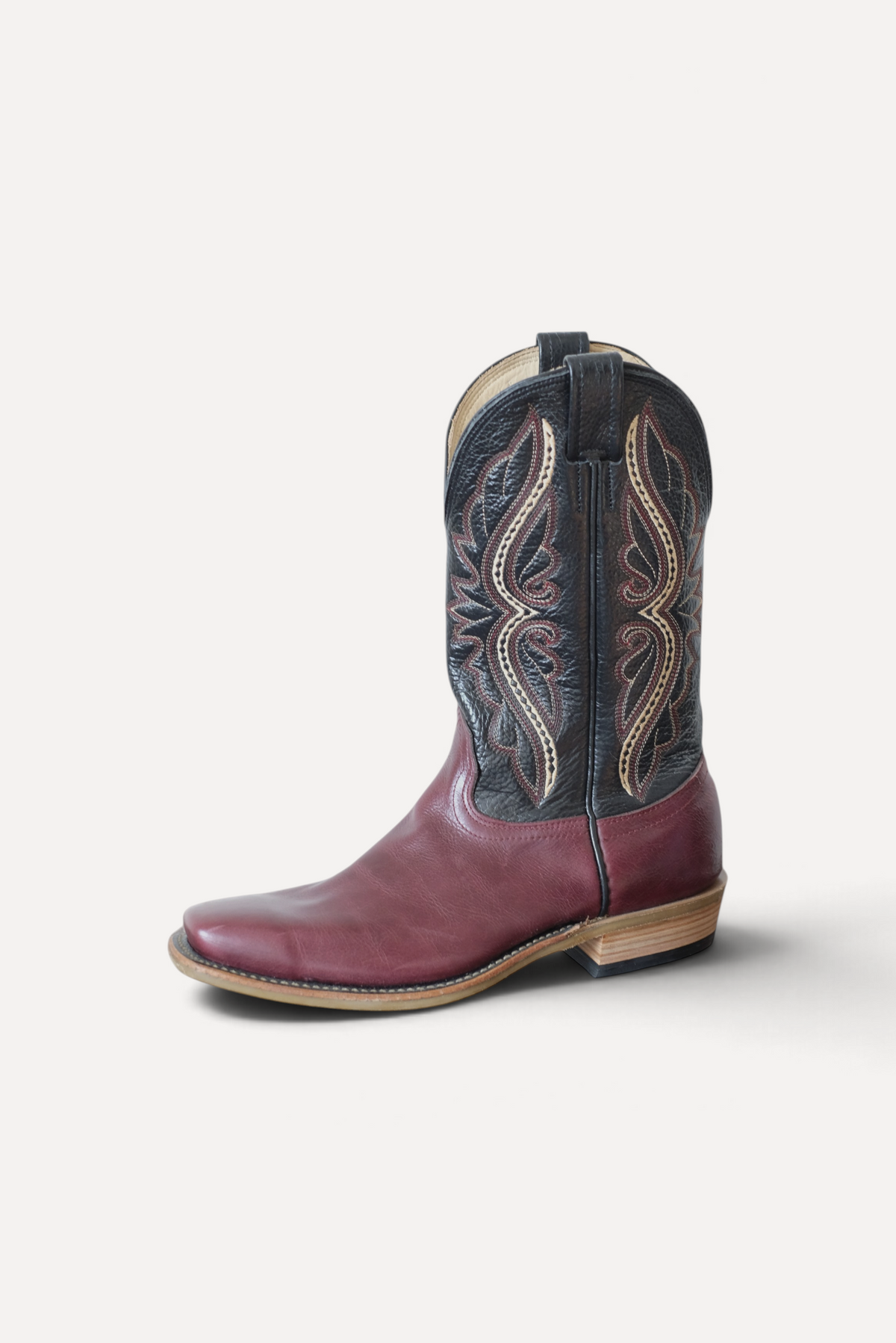 Cowboy boot with a cabernet leather vamp and black stitched top, side view