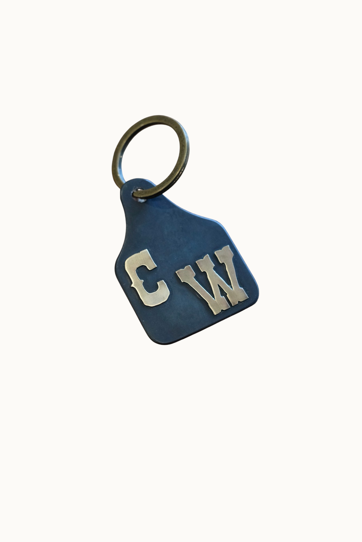 Wilkinson's Fine Goods custom steel stock tag with hand-cut brass initials on a wooden surface