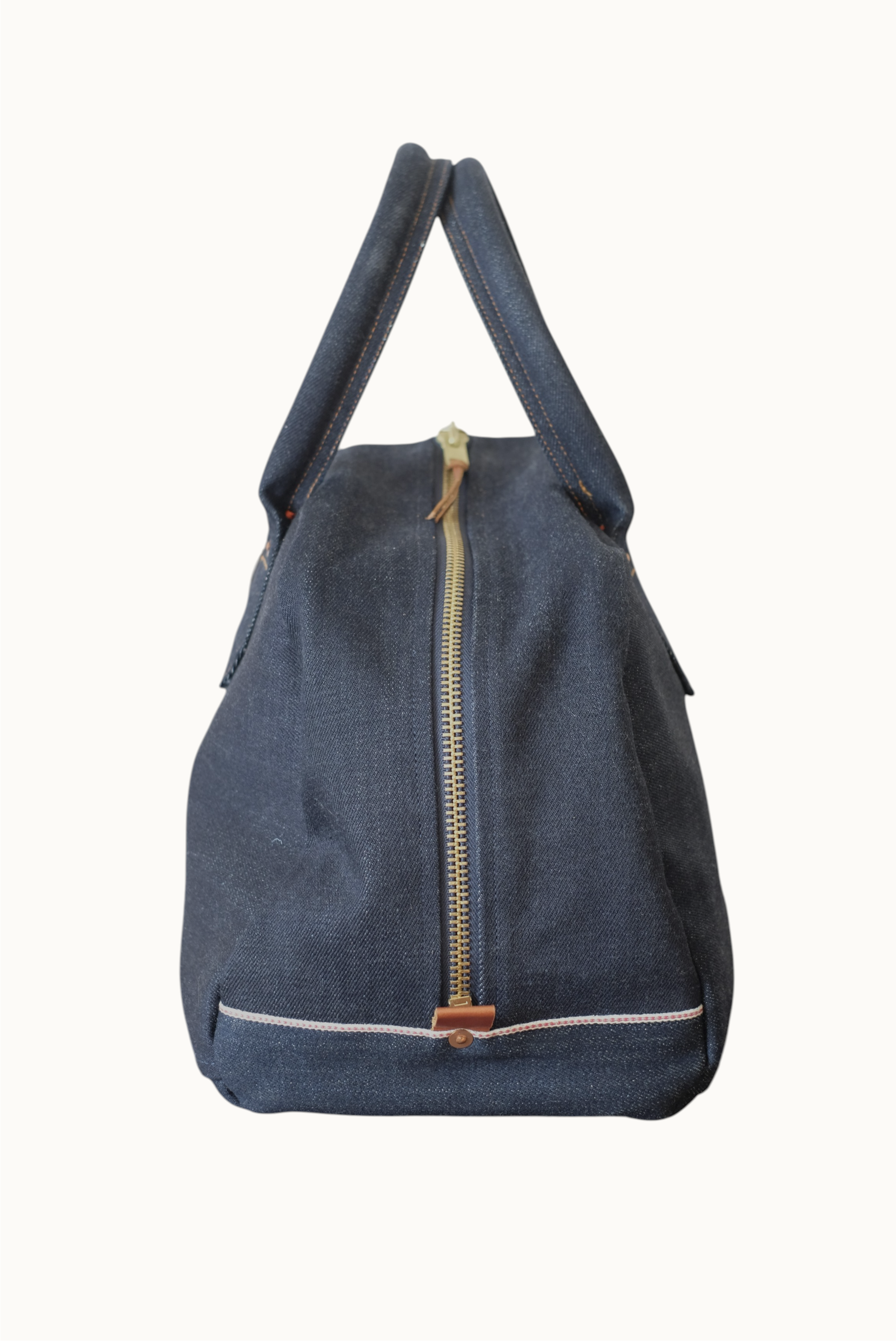 Wilkinson's Fine Goods Ciano Farmer denim weekender bag with a brass zipper and selvedge detail on a wooden surface.