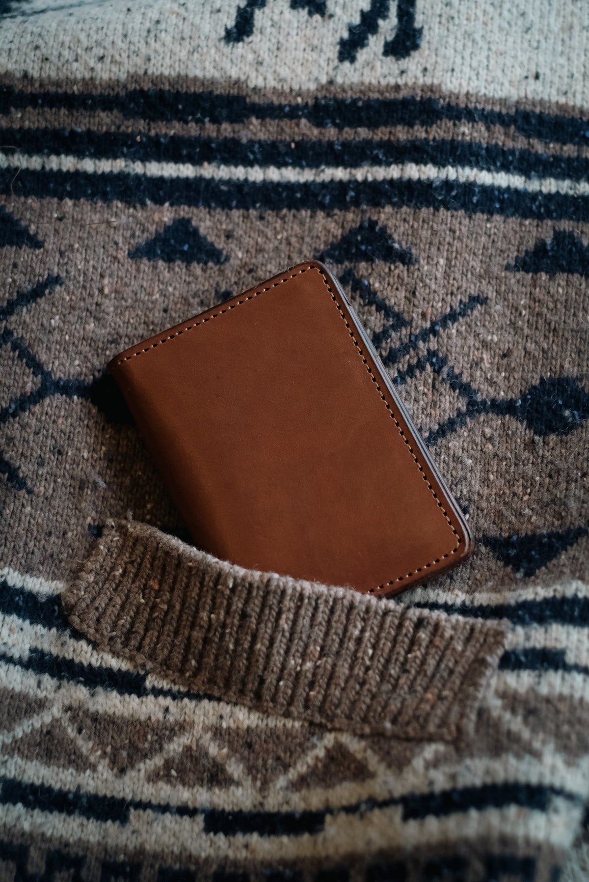 Wilkinson's Fine Goods Trinity wallet in brown full-grain leather resting in a textured knit sweater pocket