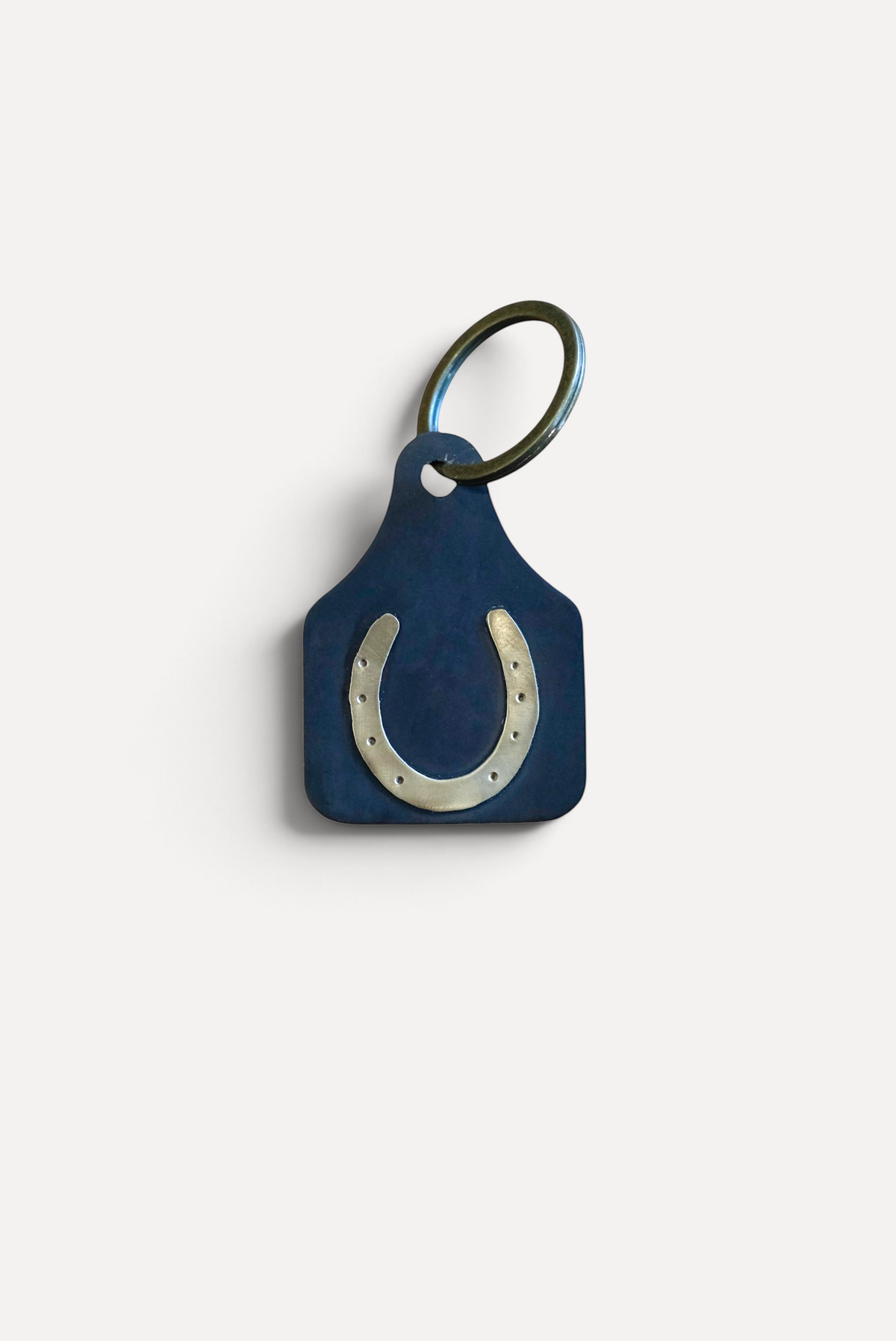 Wilkinson's Fine Goods horseshoe stock tag made from 16-gauge steel with soldered brass on a wooden surface