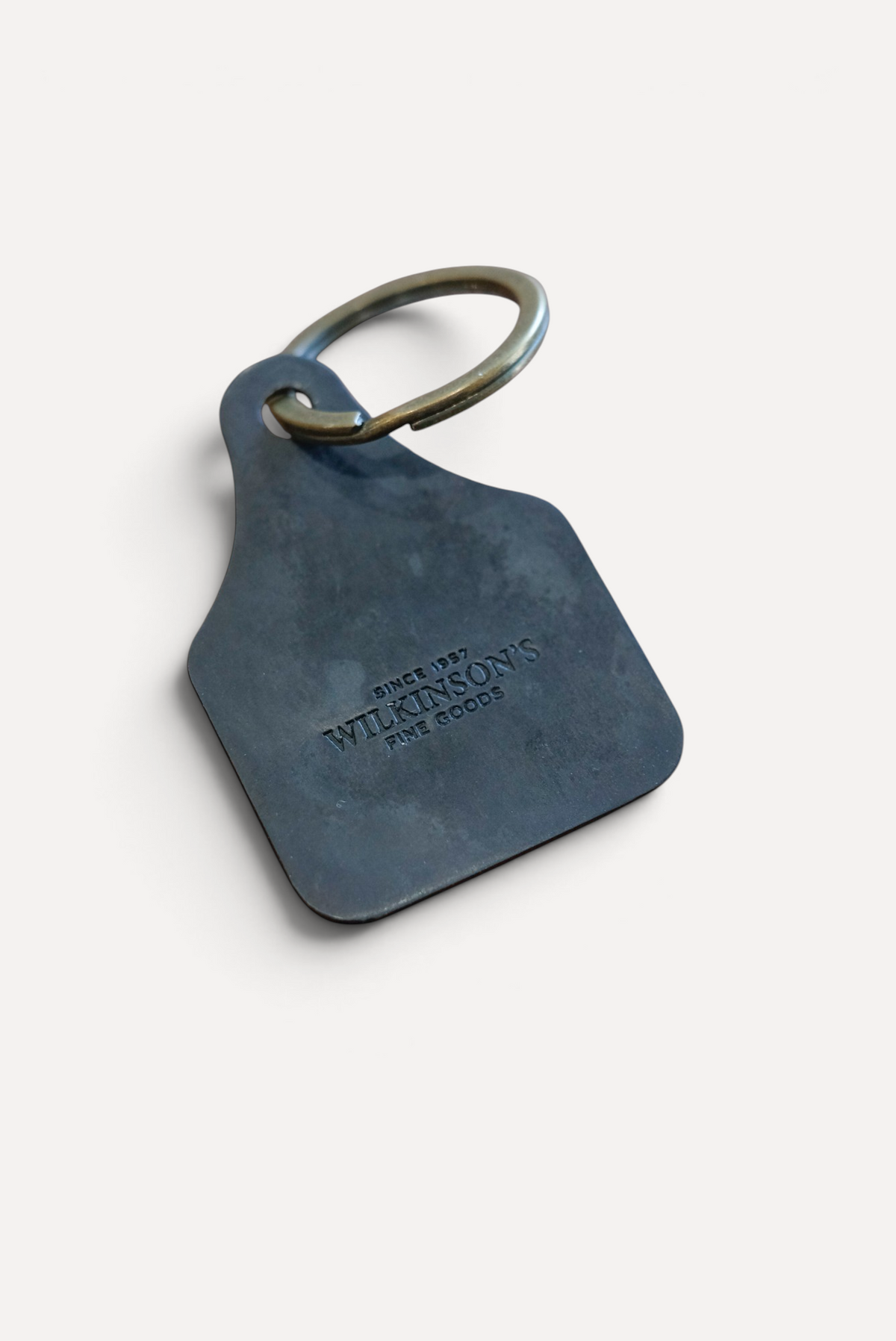 Wilkinson's Fine Goods horseshoe stock tag made from 16-gauge steel with a brass ring on a wooden surface.