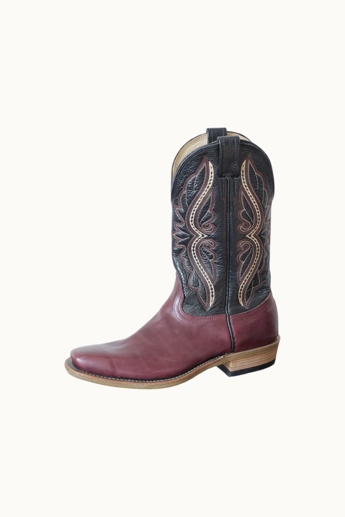 Wilkinson's Fine Goods handmade cowboy boot with cabernet leather vamp and black stitched top on a wooden surface