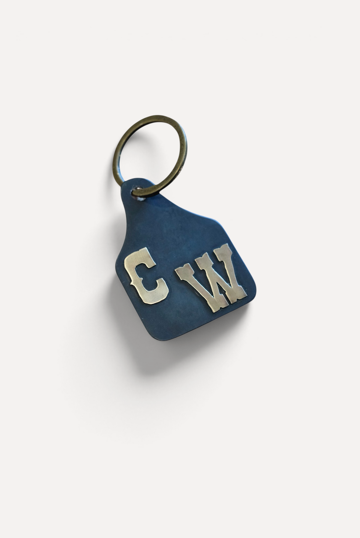 Wilkinson's Fine Goods custom steel stock tag with hand-cut brass initials on a wooden surface