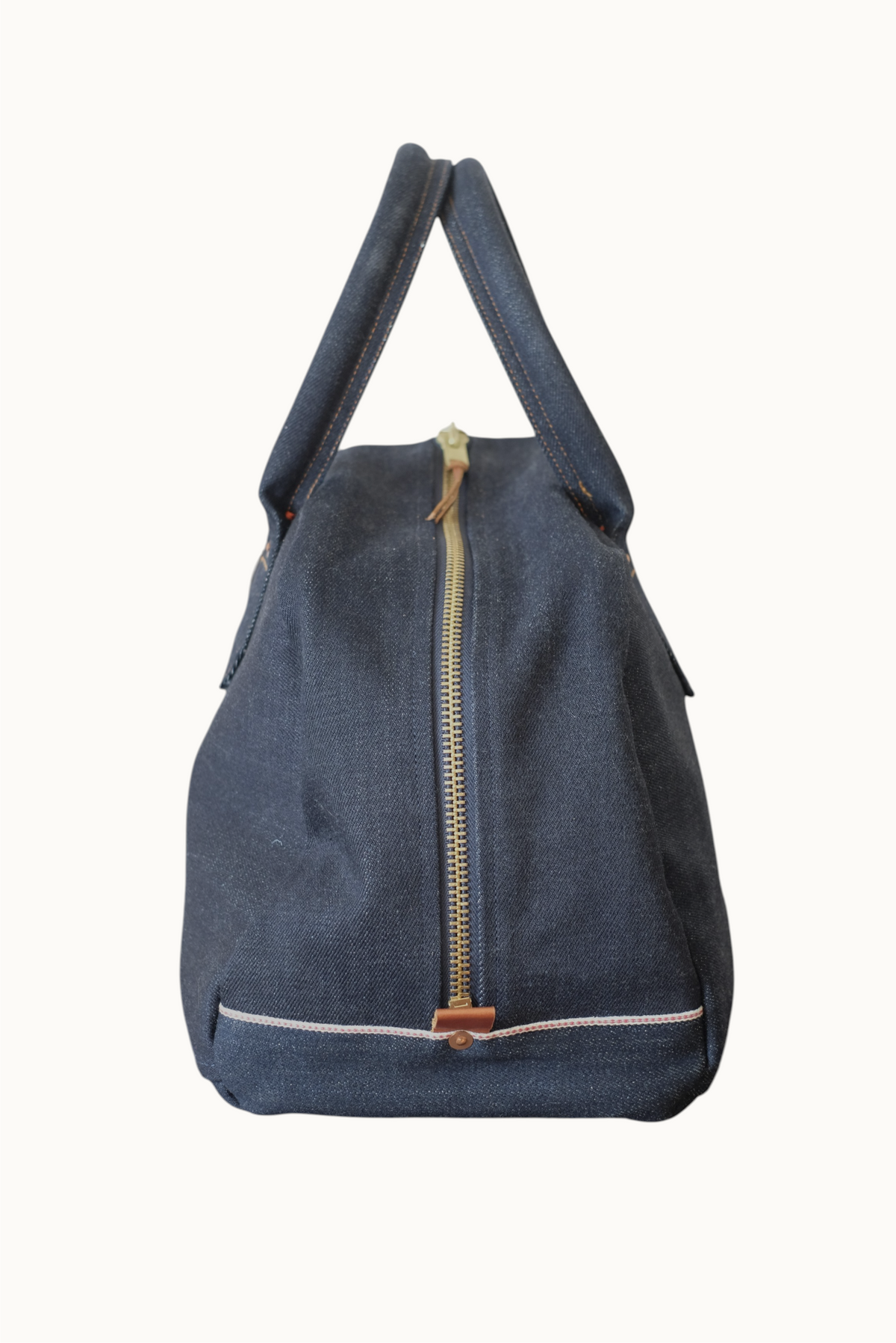 Wilkinson's Fine Goods Ciano Farmer denim weekender bag with a brass zipper and selvedge detail on a wooden surface.