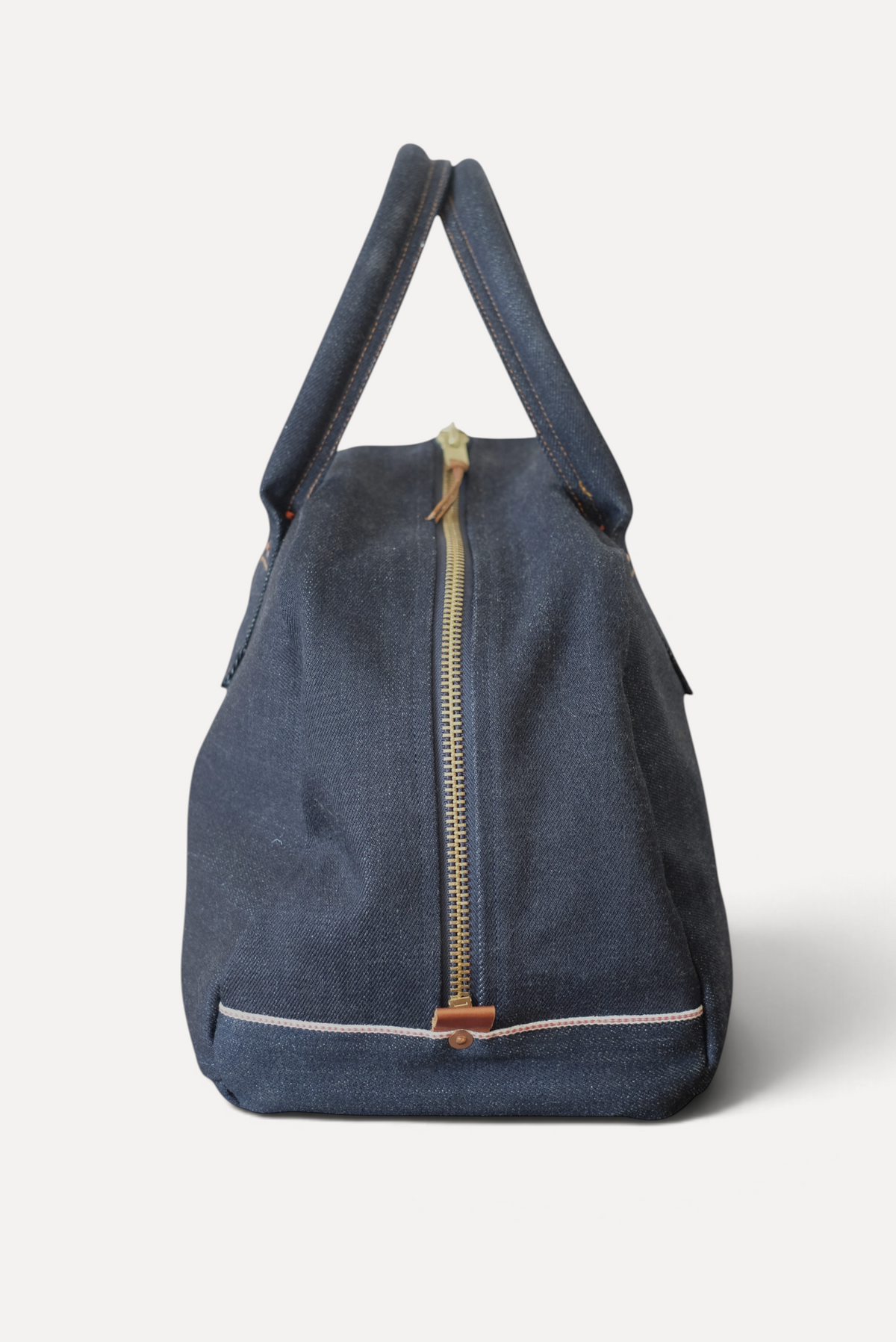 Wilkinson's Fine Goods Ciano Farmer denim weekender bag with a brass zipper and selvedge detail on a wooden surface.