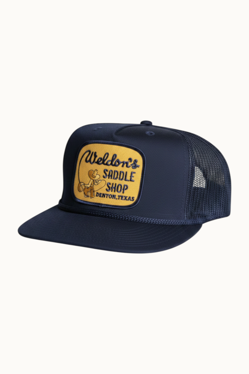 Wilkinson's Fine Goods navy trucker hat with vintage Weldon's Saddle Shop patch and rope detail on the brim.
