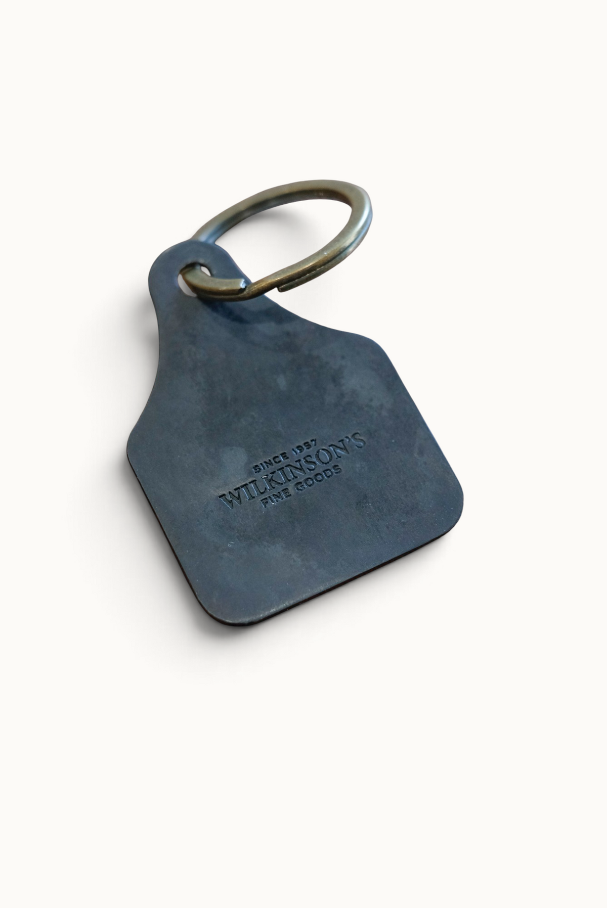 Wilkinson's Fine Goods hand-cut 16-gauge steel stock tag with a brass ring, featuring an embossed brand logo.