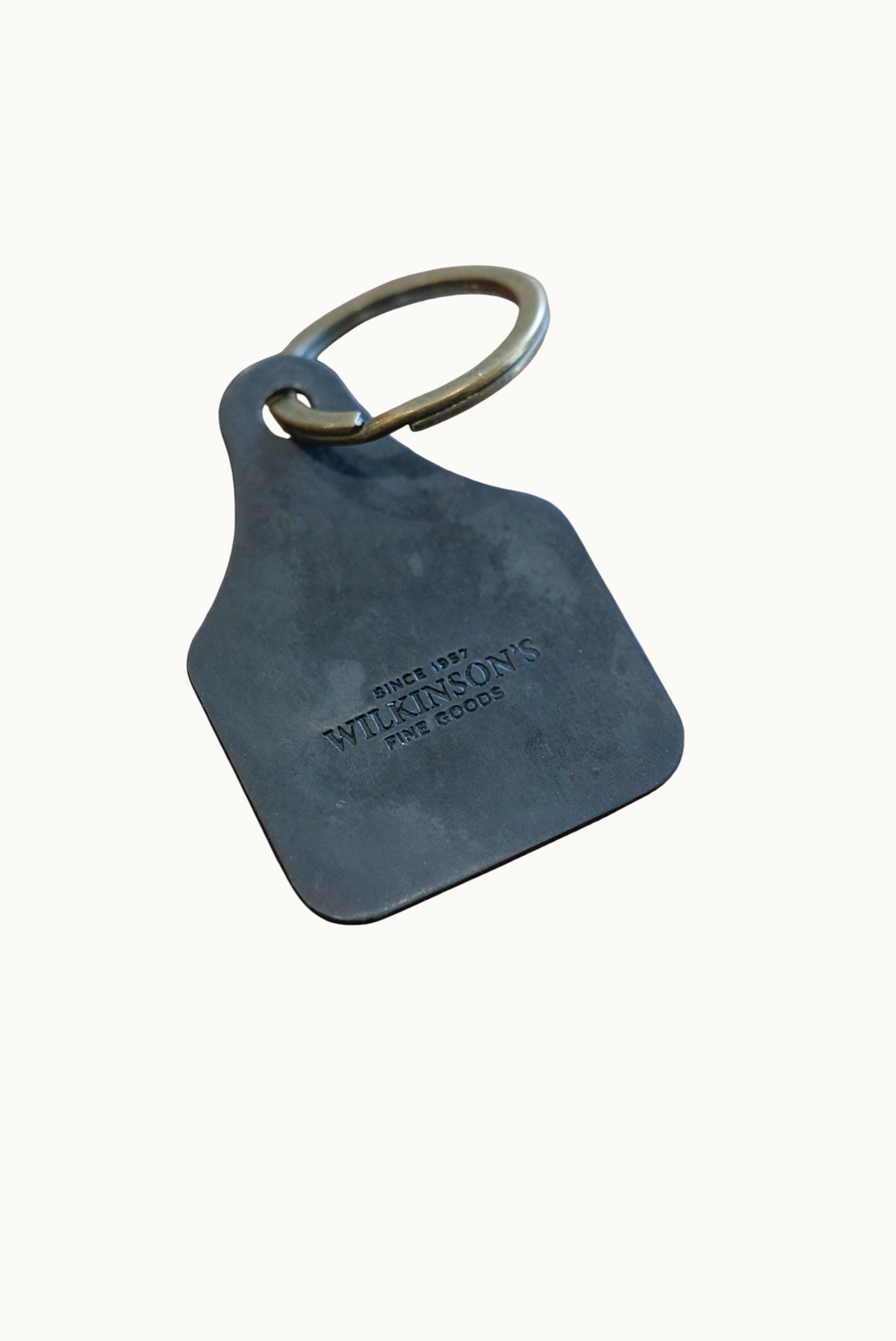 Wilkinson's Fine Goods custom steel stock tag with brass ring on a wooden surface